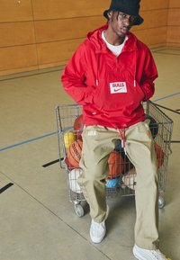Röd lättviktsanorak med "BULLS"-logotyp och Nike-märke. Beiga cargobyxor med "NBA"-detalj. Vita sneakers. Shoppingvagn fylld med basketbollar.