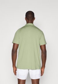 Grønn kortermet polo skjorte laget av lett stoff, med krage og rett kant, brukt med hvite shorts.