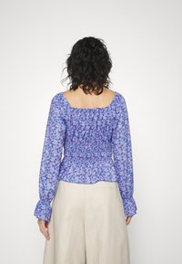 Floral Bluse in Lila und Blau, mit rüschenbesetztem Rücken, langen Ärmeln mit Rüschensaum und einem quadratischen Ausschnitt.