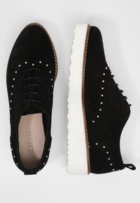 Zapatos de ante negros con suela de goma blanca, adornados con tachuelas plateadas a lo largo de la parte superior, punta redonda y diseño clásico de cordones.