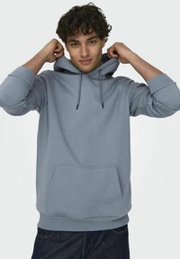 Lichtblauwe hoodie met een voorzak, trekkoord-capuchon en geribbelde manchetten. Zachte stofstructuur, losjes vallende pasvorm, casual ontwerp.