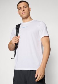 Camiseta de algodón blanca de manga corta y cuello redondo; presenta el logo azul "Peak Performance" en el pecho; textura suave.
