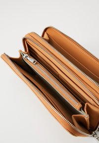 Kožená peněženka v hnědé barvě s více přihrádkami a stříbrnými zipy. Má hladký povrch a jednoduchý, funkční design.