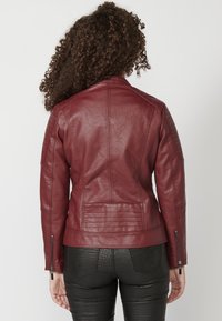Burgundowa skórzana kurtka motocyklowa z pikowanymi detalami na ramionach, zamkiem błyskawicznym przy mankietach i dopasowanym krojem, wyeksponowana z tyłu.