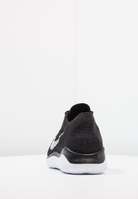 Zwarte sneaker met een gestructureerde bovenkant, ronde hak, wit logo aan de zijkant, flexibele rubberen zool en een nauwsluitende enkelpasvorm.