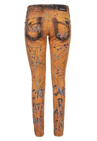Jean slim ajusté couleur tan avec éclaboussures de peinture, détails de rivets noirs, poches arrière à rabat et texte style graffiti sur les jambes et les poches.