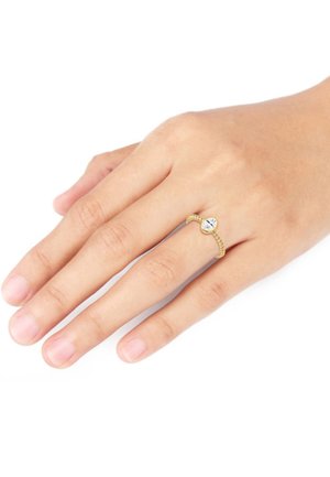 Guldtonet ring med et snoet bånddesign og en central klar ædelsten. Hånden viser naturlige negle og glat hud.