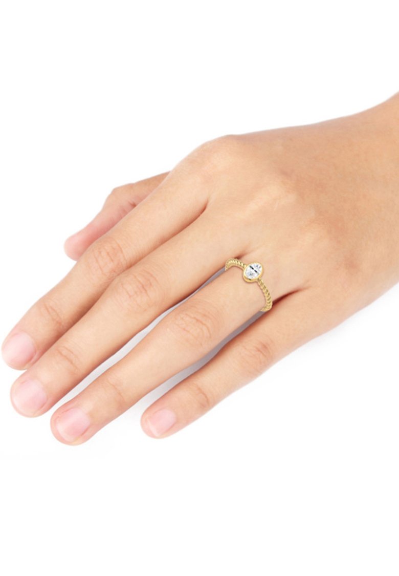 Goldfarbener Ring mit einem gedrehten Banddesign und einem zentralen klaren Edelstein. Die Hand zeigt natürliche Nägel und glatte Haut.