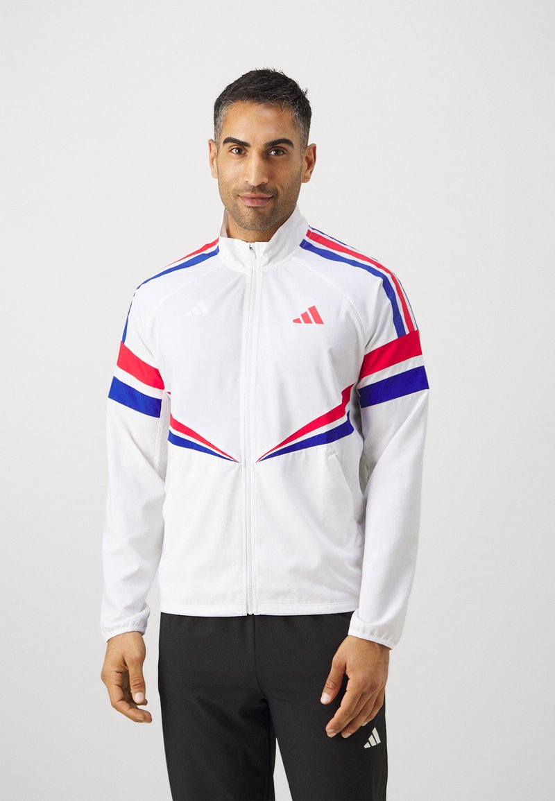 Witte sportjack met diagonale strepen in rood, blauw en roze, een volledige ritssluiting en elastische manchetten. Merklogo op de borst en de mouw.