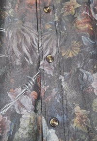 Hemd mit Knopfleiste, das einen floralen Druck in verschiedenen Farben auf einem dunkelgrauen Hintergrund zeigt. Verfügt über goldfarbene Knöpfe und feine Nähte.