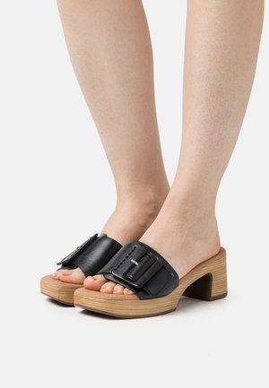 Sandali in pelle nera con una larga fascia caratterizzata da una grande fibbia, montati su un tacco in legno. Design open-toe in evidenza.