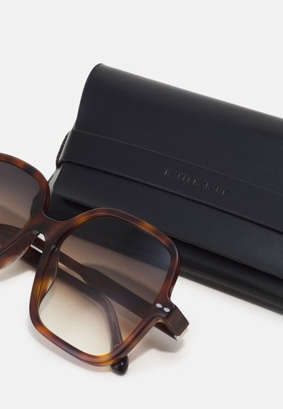 Lunettes de soleil oversize en écaille de tortue marron avec verres dégradés placées à côté d’un étui en cuir noir embossé de "Isabel Marant."
