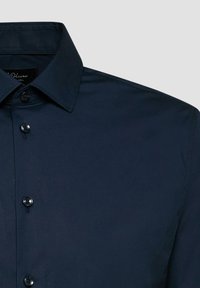 Chemise bleu marine foncé à boutons avec col pointu et coutures visibles sur la couture d'épaule.