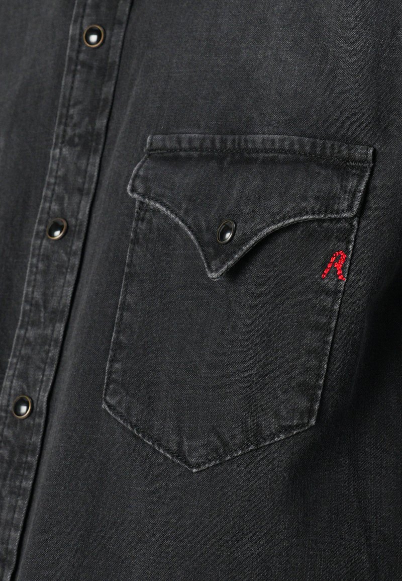 Czarna koszula dżinsowa z kieszenią na piersi z zaokrągloną klapką, czarnymi guzikami i małym, czerwonym haftowanym logo na kieszeni.