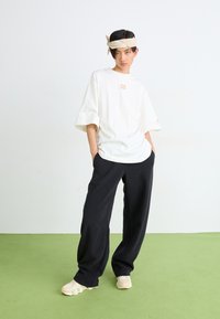 Fehér, oversize t-shirt bordás textúrával és diszkrét "23" logóval, fekete, széles szárú nadrággal és krém színű, vastag talpú sneakers-szel párosítva.