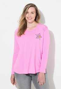Camicia a maniche lunghe rosa realizzata in tessuto morbido, con una grafica a stella in grigio e giallo, e cuciture decorative sulla cucitura della spalla.