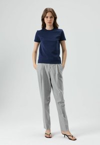 Marineblauw T-shirt met korte mouwen en een ronde hals, gecombineerd met lichtgrijze, op maat gemaakte broek. Model draagt zwarte sandalen met bandjes; minimalistisch ontwerp.