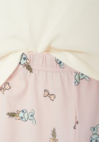 Hellbeige Oberteil mit gerafftem Stoff über einem pinken Unterteil mit cartoonhaften Motiven von Hasen mit Schleifen und Ananas, Baumwolltextur.