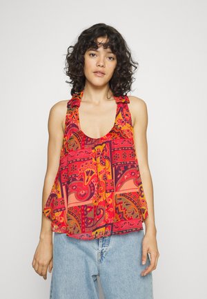 Top sem mangas em padrão vermelho e laranja com decote redondo, alças com babados e corte solto, combinado com jeans de perna larga em azul claro.