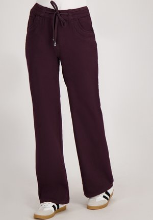 Donkerpaarse rechte broek met voorzakken en een drawstring taille, gedragen met witte sneakers met zwarte strepen.