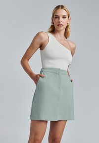 Gonna sartorial verde chiaro con tasche laterali, tessuto liscio, design semplice e taglio dritto, abbinata a un top bianco a spalla singola con righe.