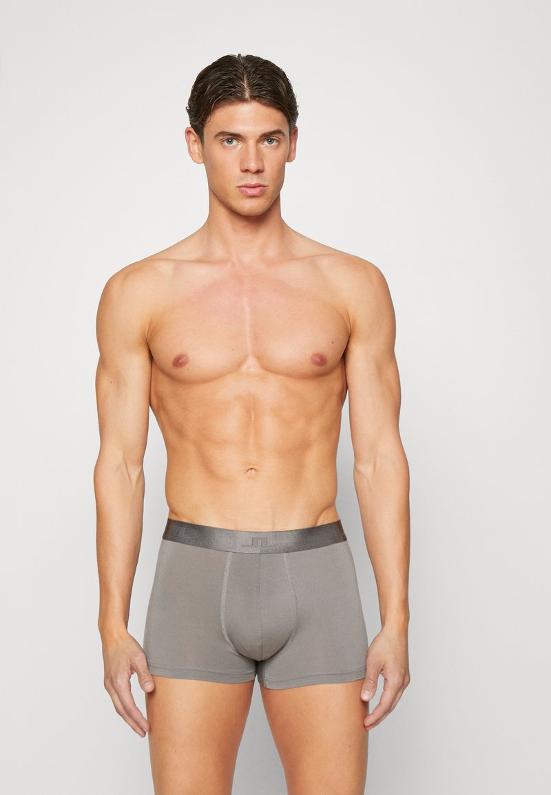 Grå boksershorts med myk tekstur, elastisk midje, og logo detalj, vist på en mannlig modell med muskuløs physique.
