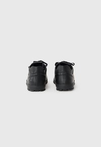 Black athletic shoes with a smooth leather upper, textured rubber sole, and flat laces. Features pairs of eyelets and a rounded toe design.