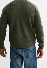 Maglione a maglia verde oliva con texture a coste, maniche lunghe, scollatura a girocollo, abbinato a jeans in denim blu con tasche posteriori.