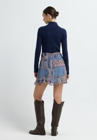Marineblauwe geribde trui, gestreepte blauwe rok met ruches, en bruine knielange laarzen. De rok heeft paisley- en stippenontwerpen.