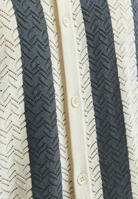 Cardigan lavorato a maglia con motivi a zigzag alternati in blu navy e crema, con piccole chiusure a bottone e un tessuto testurizzato.