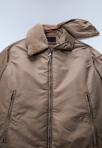 Brązowa pikowana kurtka z beżowym kołnierzem z sztucznego owczego futra, bocznymi kieszeniami na zamek błyskawiczny i zapięciem z przodu na zamek. Gładka faktura, lekka konstrukcja.