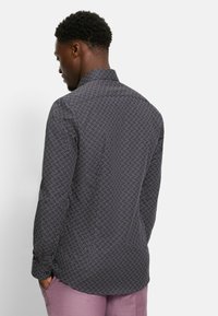 Camicia a maniche lunghe con un motivo scuro che presenta un design geometrico in tonalità di blu e rosso, con colletto a punta.