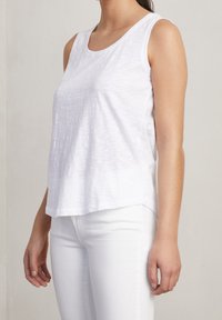 Top bianco senza maniche realizzato in tessuto leggero con una texture morbida. Presenta un collo rotondo e una vestibilità rilassata, abbinato a pantaloni bianchi.