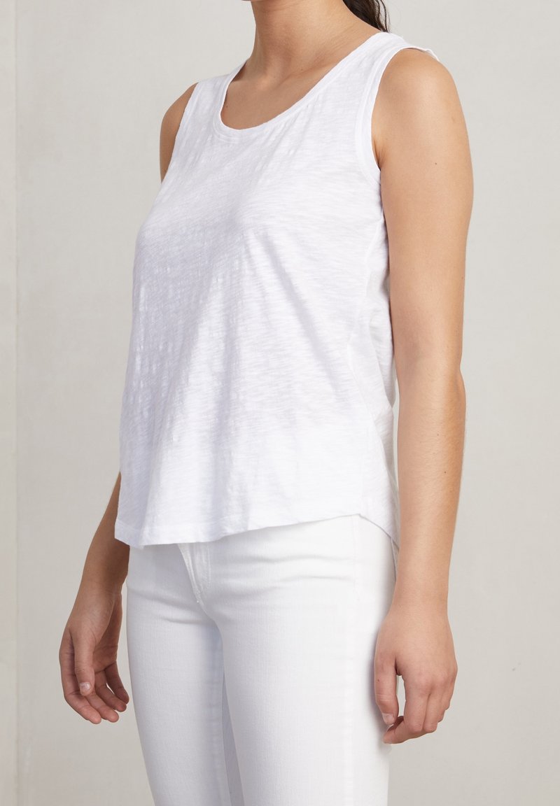 Top bianco senza maniche realizzato in tessuto leggero con una texture morbida. Presenta un collo rotondo e una vestibilità rilassata, abbinato a pantaloni bianchi.