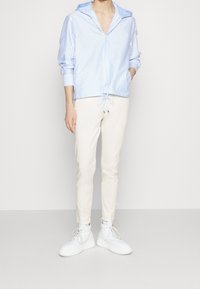 Jasnoniebieska i biała koszula zapinana na guziki w paski z wiązanym paskiem w talii, zestawiona z kremowymi spodniami o wąskim kroju i białymi trampkami.