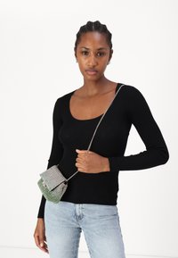 Svart ribbet langermet topp kombinert med lyseblå jeans; holder en liten, glitrende grønn og sølv farget crossover-veske med kjedehåndtak.