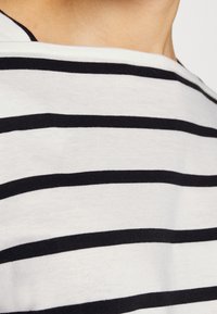 White shirt with bold black horizontal stripes, featuring a wide neckline and soft, smooth cotton texture. Design is casual and versatile.