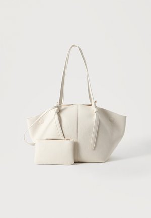 Cremefarbene, strukturierte Lederhandtasche mit zwei langen Griffen und einer passenden kleinen Reißverschlusstasche vorne, auf einfachem Hintergrund.