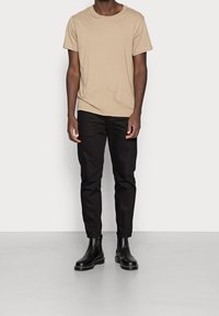 Beige cotton t-shirt with short sleeves, paired with black fitted pants. Black ankle boots with a smooth finish and thick sole. Minimalist style.