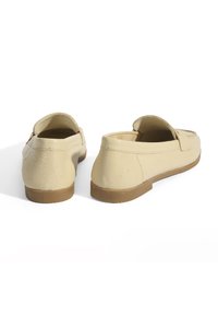 Beige leren loafers met een gestructureerd oppervlak, ronde neus en platte zool. Kenmerken zijn een lage achterkant en minimale stikselaccenten.