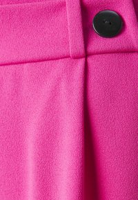 Tissu fuchsia avec une finition texturée, présentant un devant plat et un bouton noir en accent à la taille. Lignes épurées et design ajusté.