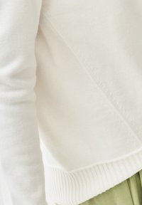 Bílý svetr s texturovaným pletením, s ribbed lemem a vyšitými detaily podél švů. Měkká, mírně elastická látka.
