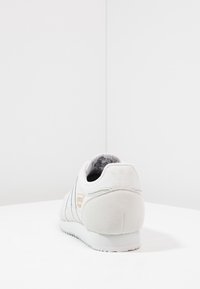 Weiße Wildleder- und Leder-Sneaker mit einer strukturierten Ferse und drei schwarzen Streifen. Verfügt über ein kleines oranges Logo an der Seite und eine Gummisohle.