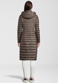 Pitkä huppu ja toppatakki ruskeana, jossa on tikattu kuvio. Ominaisuuksina kapea siluetti ja sivutaskut, yhdistettynä valkoisiin legginsseihin ja tennareihin.