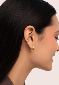 Gold hoop earrings displayed in the ear, featuring a twisted design on the upper lobe. Smooth texture with a polished finish.