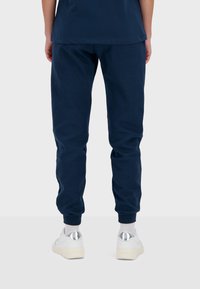 Pantaloni joggers in cotone blu navy con un design affusolato, vita elastica e polsini a costine. Abbinati a sneakers bianche con dettagli argentati.