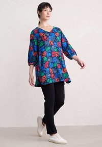 Túnica colorida y con estampado en azul, verde, rojo y negro, con mangas de tres cuartos, escote en V y aberturas laterales, combinada con pantalones negros y zapatillas blancas.