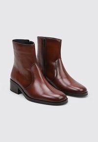 Bottines en cuir marron avec une finition lisse, dotées d'une fermeture éclair sur le côté et d'un petit talon bloc. Pas de motifs ni d'accents marquants.