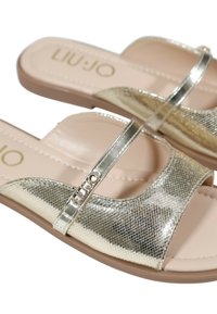 Sandali a slide metallici dorati con una finitura testurizzata, punta aperta e una sottile cinghia con dettaglio del logo. Soletta beige morbida e suola flessibile.