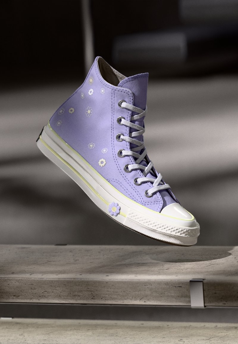 Purple canvas high-top sneaker with floral embroidery, white rubber toe cap, and sole with yellow accent. Laces in the front, lightweight design.